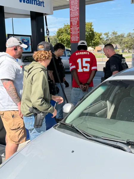 Group standing beside a car near a storefront in daylight.