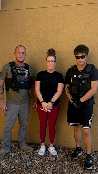 Three people standing against a tan wall.