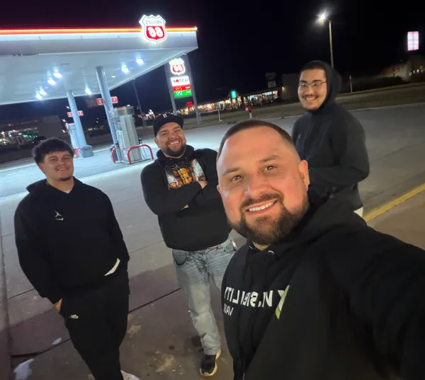Group selfie outside a gas station at night.