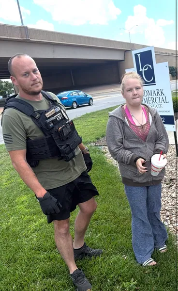 Two people standing on grass near a commercial building.