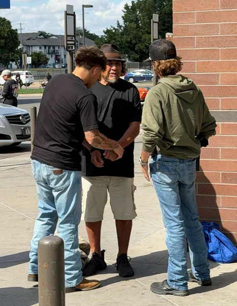 Three people standing beside a brick wall near a sidewalk.