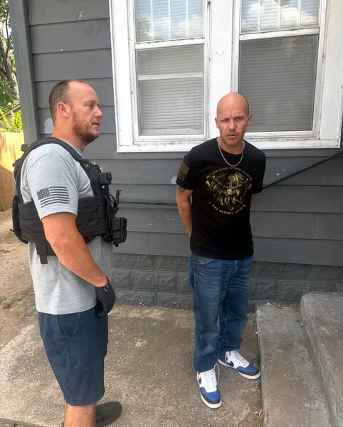 Two people standing outside a gray house.