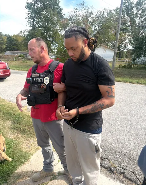 Two people standing outdoors beside a driveway.